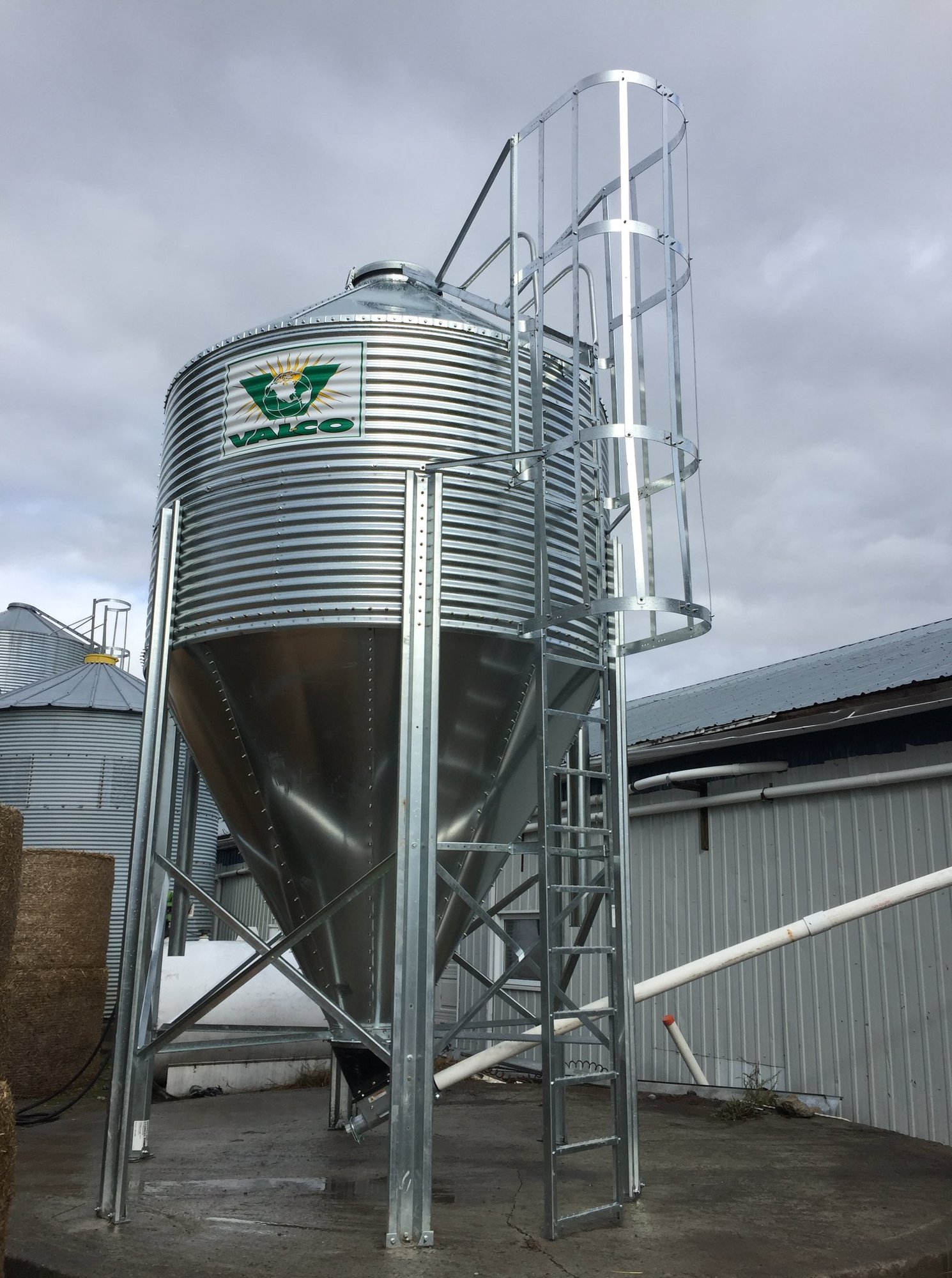 Silo à grain VALCO sur cône (trémie) galvanisé installé par CFI Industrie chez un producteur agricole québécois — échelle de service avec garde-corps cylindrique et vis sans fin de distribution