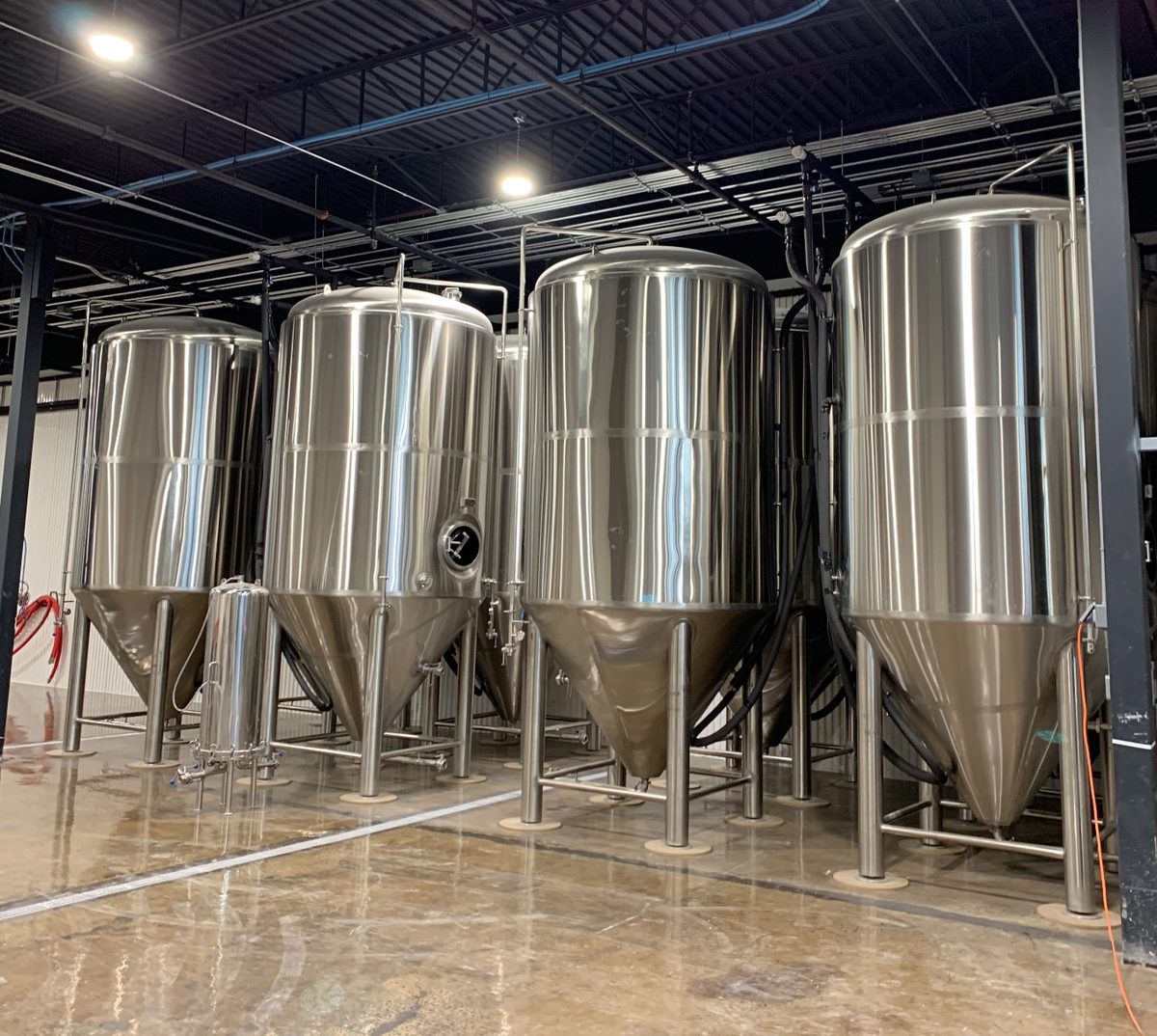 Four 304 stainless steel conical fermenters aligned in the brewing room of Malco Brewery in Quebec — installation and sanitary welding by CFI Industries